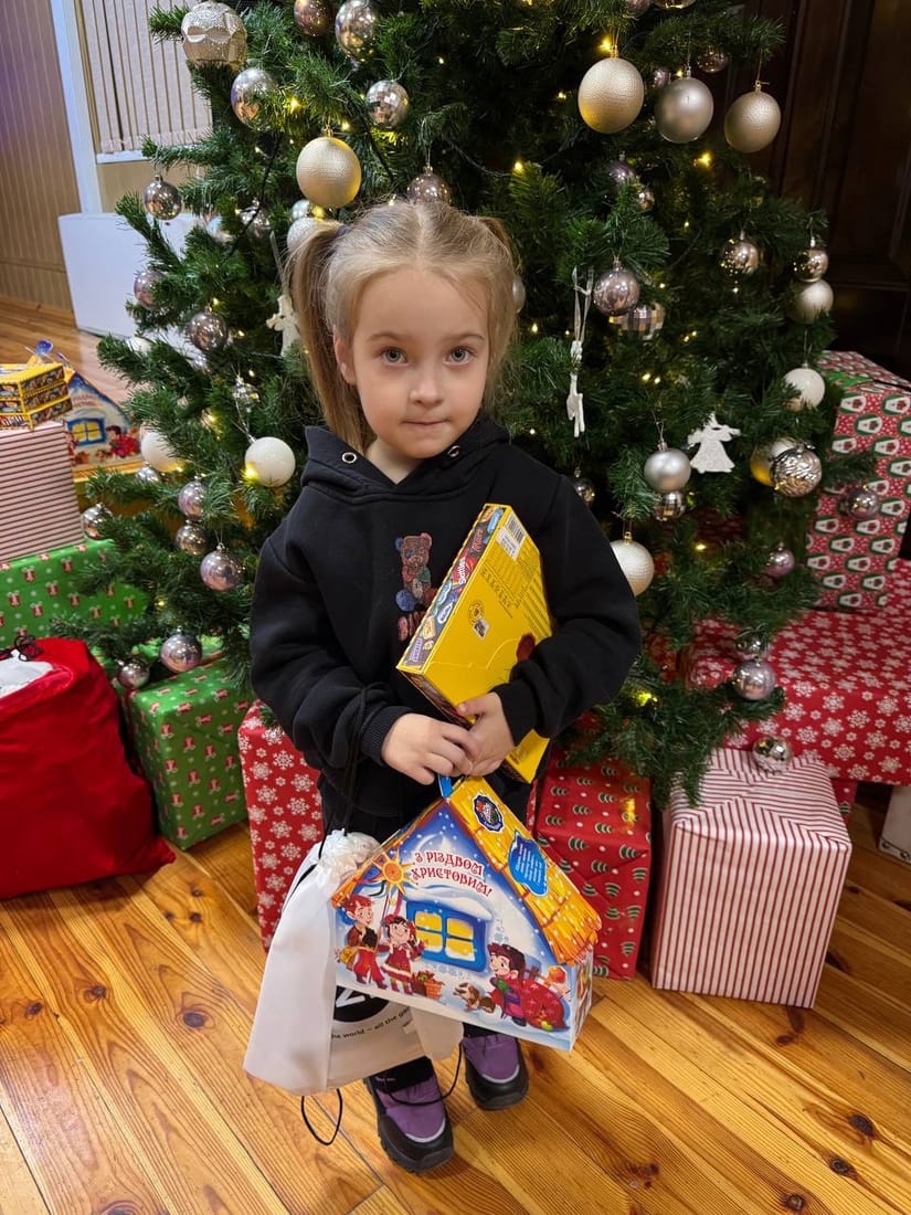 A little girl in Ukraine holding her Christmas gift by the tree